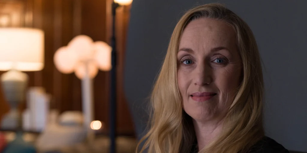 Smiling person with long blonde hair in warmly lit room, suggesting a welcoming and professional environment