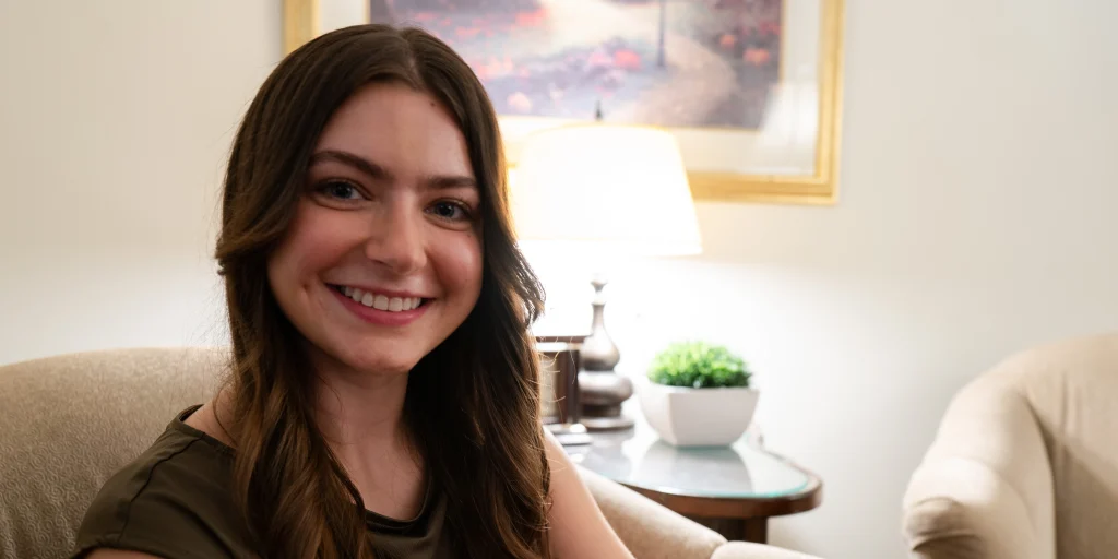 Smiling woman seated in a warmly lit counseling office with a painting and lamp in the background